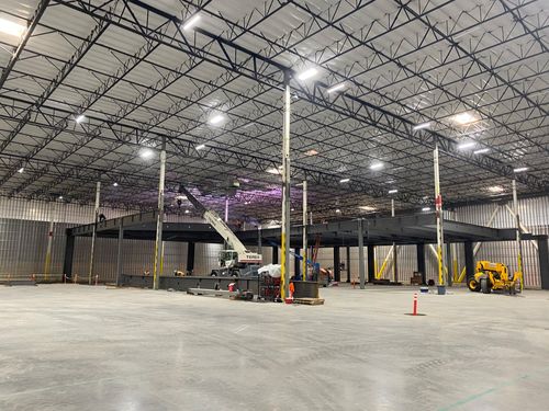 A crane installing new steel framing inside an existing warehouse.