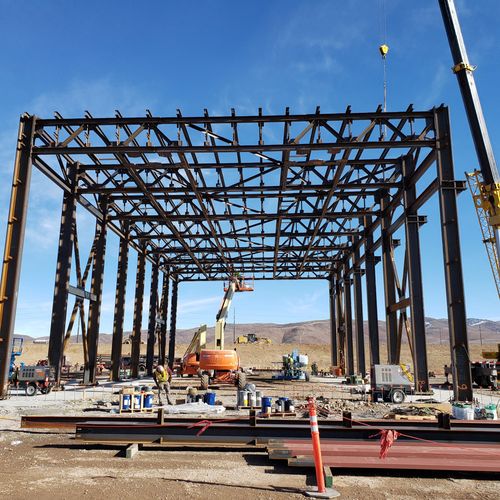 A steel frame being constructed with cranes and boom lifts