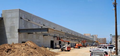 Various equipment outside a warehouse building installing steel shade structures.