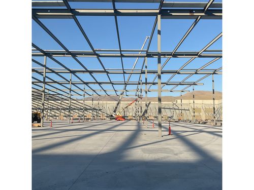 A crane and a boom lift lifting steel girders into place for a warehouse roof.